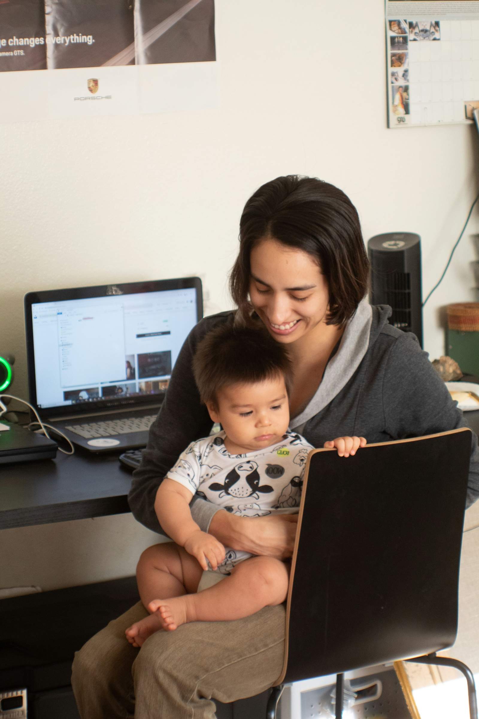 Mujer sonriendo con su bebé en brazos frente al computador